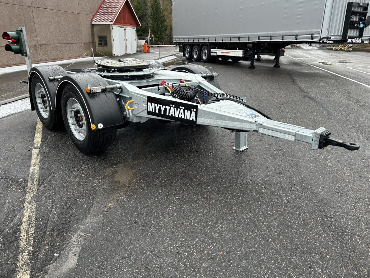 Kaksipyöräinen teräsrunkoinen perävaunu on pysäköity asfaltille. Kehyksessä on kyltti, jossa lukee Myytävänä. Taustalla isompi ajoneuvo ja perävaunu.