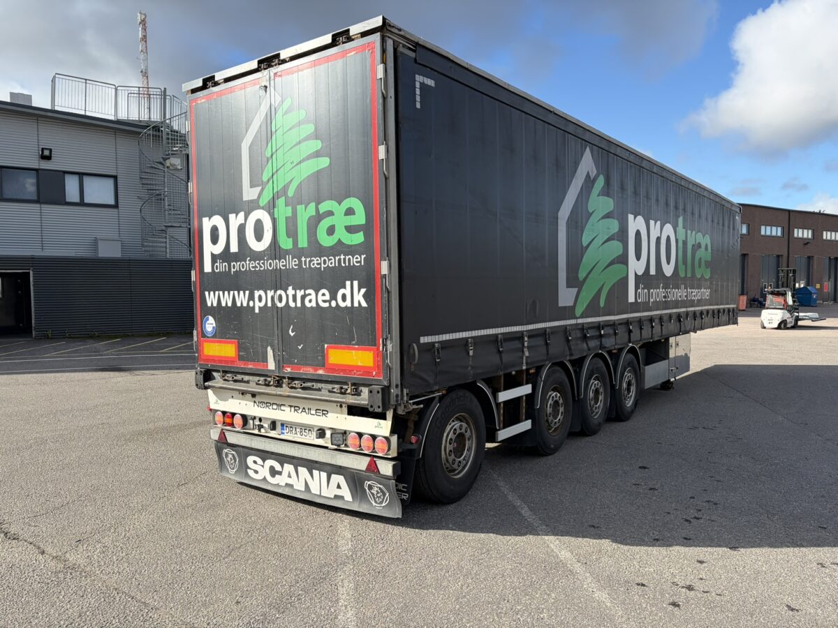 Suuri Scania-kuorma-auto, jonka perävaunussa lukee ”protrae”, on pysäköity teollisuusalueelle osittain pilvisen taivaan alla. Perävaunussa on vihreä-valkoisia grafiikoita ja tanskankielistä tekstiä.