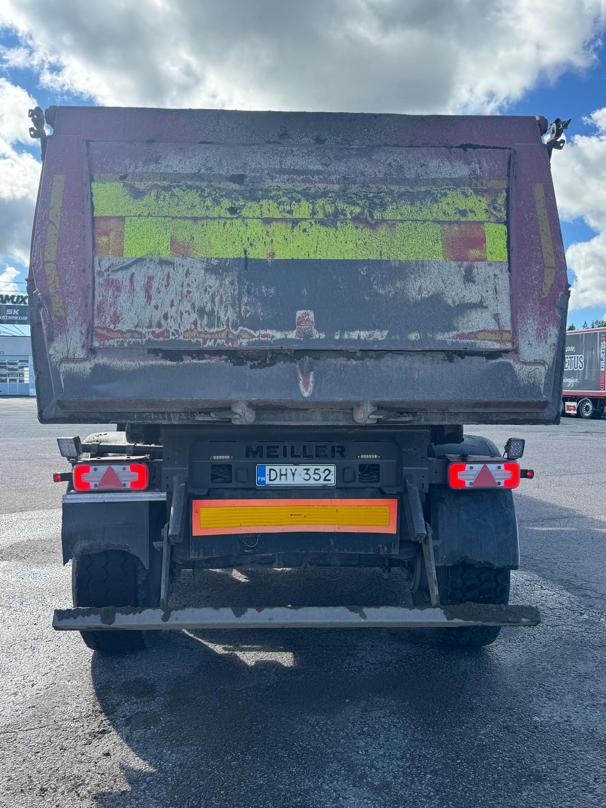 Takapuolelta kuvattu suuri kippiauto, jonka takapinta on likainen ja sään kuluttama, ja jossa on keltaisia ja punaisia heijastavia merkintöjä sekä rekisterikilpi DHY 352. Auto on pysäköity asfalttipinnalle osittain pilvisen taivaan alla.