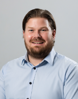 Partainen mies, jolla on yllään vaaleansininen kauluspaita, hymyilee kameraan.
