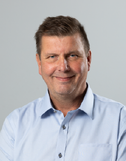 Lyhyttukkainen, hymyilevä keski-ikäinen mies, jolla on vaaleansininen napituspaita.