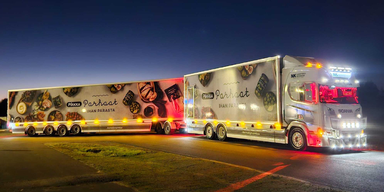 Yöllä pysäköity hopeanvärinen Scania-rekka ja perävaunu, joissa molemmissa on Pirkka Parhaat -ruokabrändin kuvia ja tekstiä.